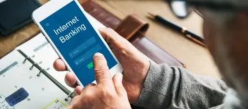 Hands holding a phone with an internet banking app over financial papers