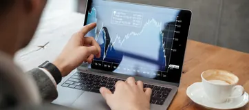 A laptop showing stock market charts next to a cup of coffee