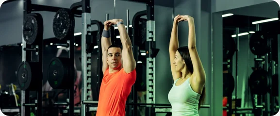 Two people stretching after a workout in a gym