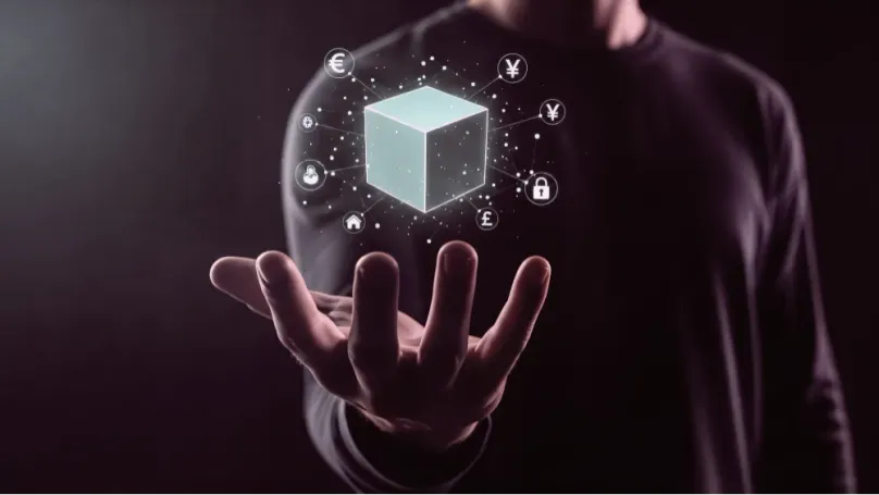 Hand holding a glowing blockchain cube with currency symbols